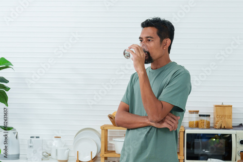 Asian man wearing comfortable pajamas on holiday morning, this man raised his glass drink clean water which poured out jug, It was jug in whic filtered water for drinking. photo
