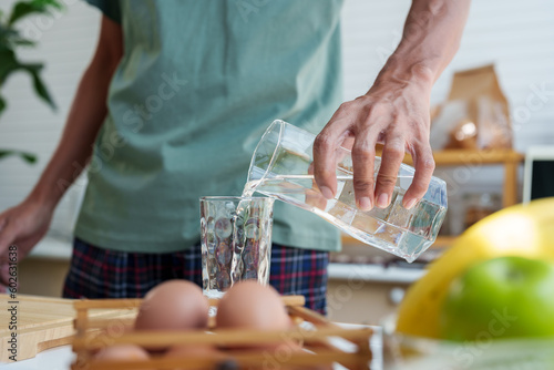 Obraz na plátně Close-up man's hands, handle pitcher, pouring clean water from pitcher into glass, in sufficient quantities drink in order drink it all in one go, after pouring, bring pitcher back its original place