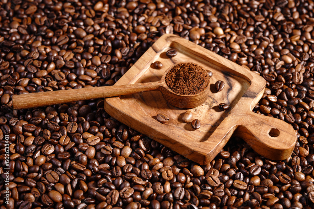 Fototapeta premium Palone ziarna kawy z drewnianym podstawkiem i łyżeczką z mieloną kawą