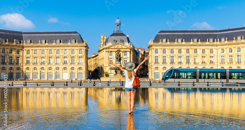 Happy woman tourist with arms raised in France- Bourse square with water mirror,  Bordeaux city landscape photo