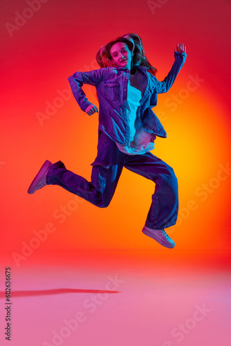 Portrait of emotive, young girl wearing casual clothes jumping in air over red color studio background in neon light. Levitating dreamer
