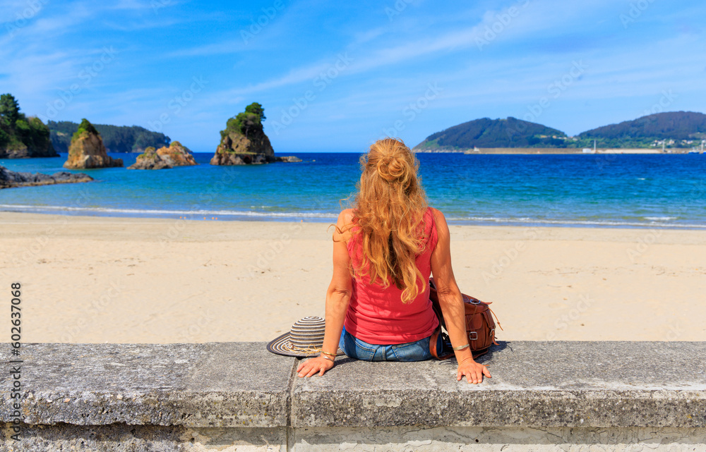 Woman sitting and enjoying panorama view of beach and rock formation- Spain