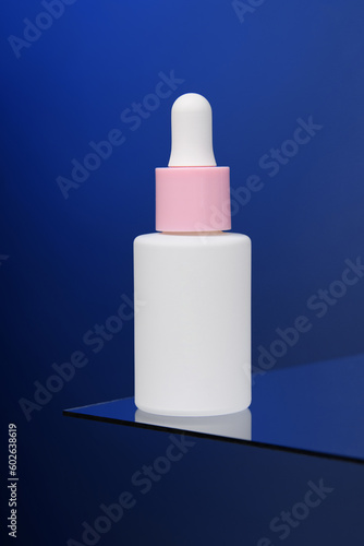 In the blue background, a bottle of serum stands on glass.  Vertical advertising photo of cosmetics. Mockup. Template.
