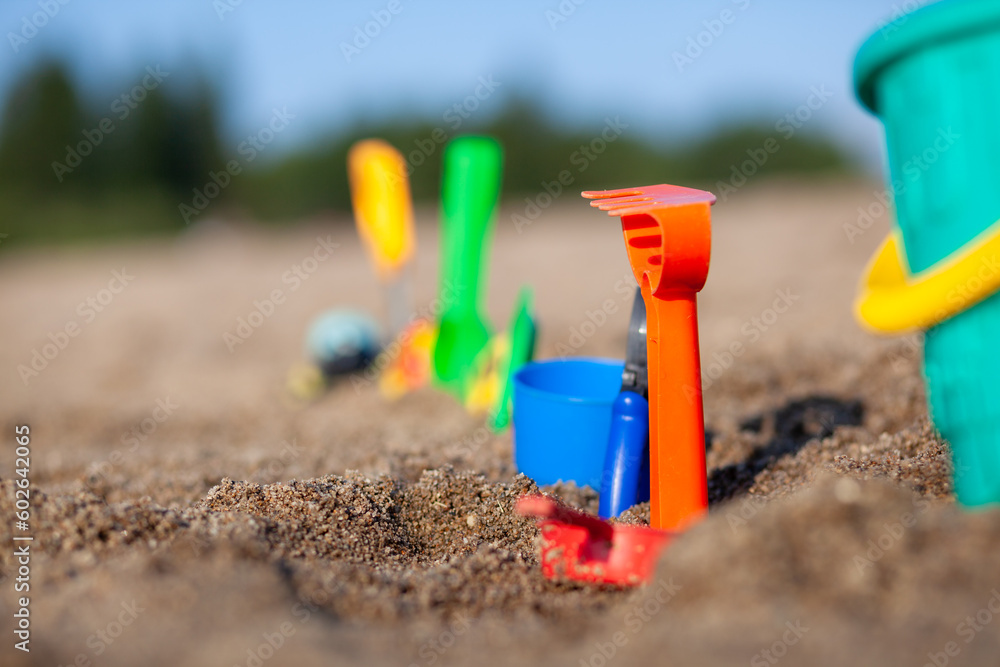 Children's toys for playing on the sand. Plastic bucket and rake on the beach at sunset. The concept of summer, family holidays and vacations. Various plastic toys for children. Children's toys for playing on the sand. Plastic bucket and rake on the beach at sunset. The concept of summer, family holidays and vacations. Various plastic toys for children.