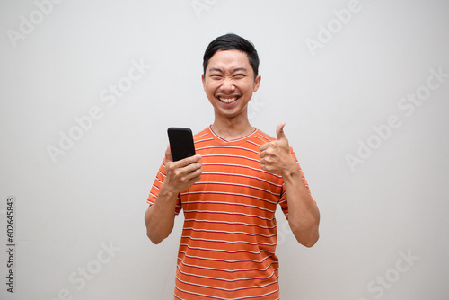 Asian man orange shirt feels happy holding mobile phone and show thumb up isolated
