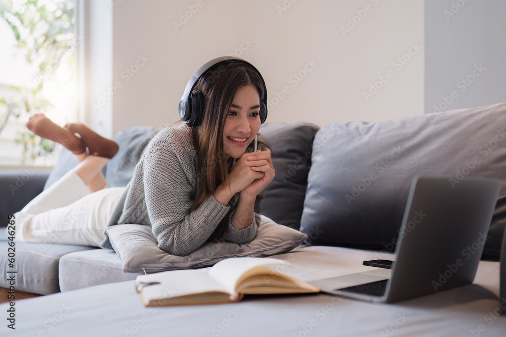 Online education, e-learning. Asian woman in stylish casual clothes, studying using a laptop, listening to online lecture, taking notes, online study at home Online education, e-learning. Asian woman in stylish casual clothes, studying using a laptop, listening to online lecture, taking notes, online study at home