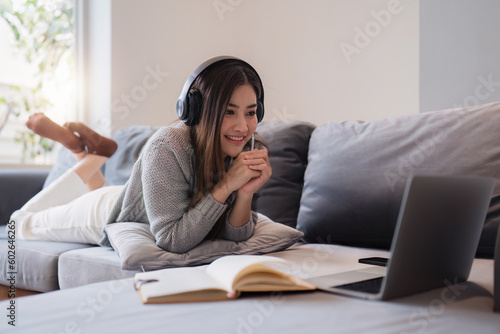 Online education, e-learning. Asian woman in stylish casual clothes, studying using a laptop, listening to online lecture, taking notes, online study at home