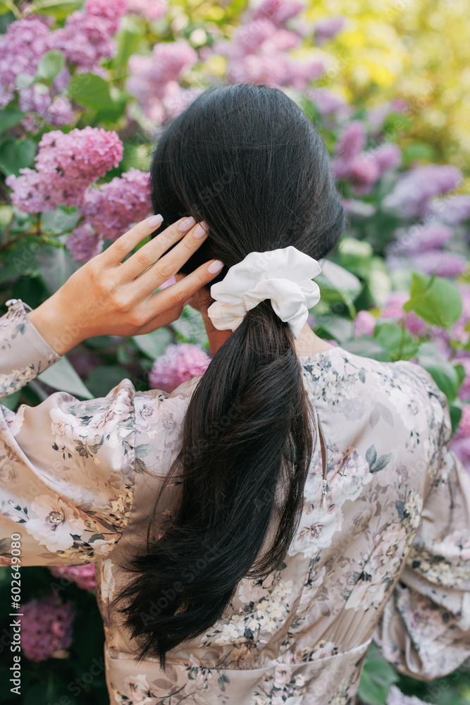 Naklejka premium Back view to brunette woman enjoying by blooming lilac shrubs.