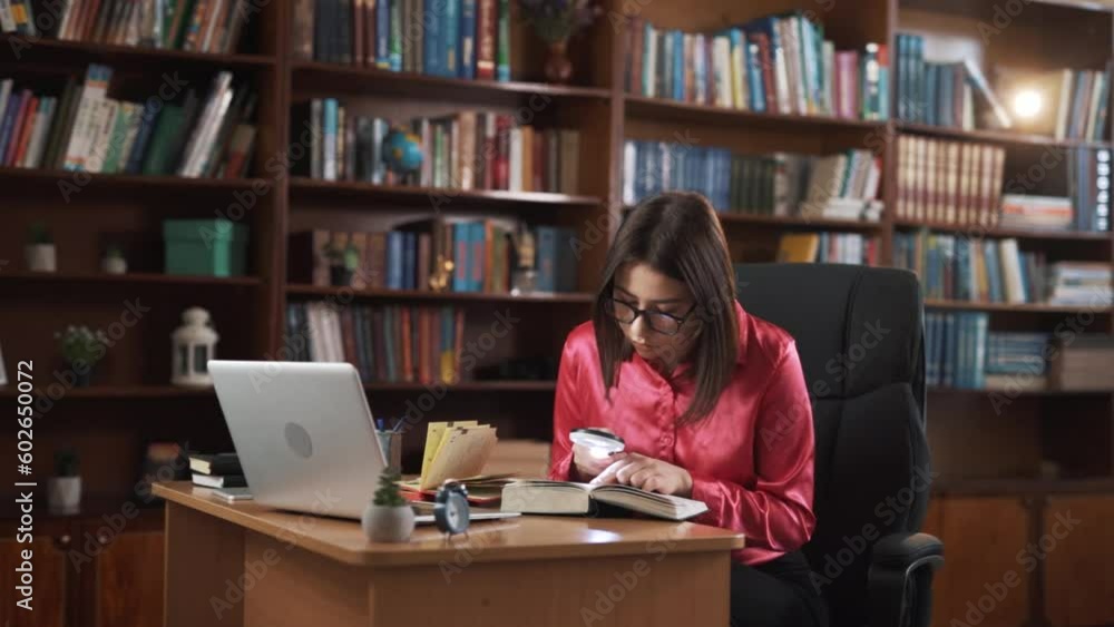 The girl is sitting at her workplace, reading a book with great concentration. She is holding an object that resembles a magnifying glass, and she is also lighting the text for herself. The girl is sitting at her workplace, reading a book with great concentration. She is holding an object that resembles a magnifying glass, and she is also lighting the text for herself.