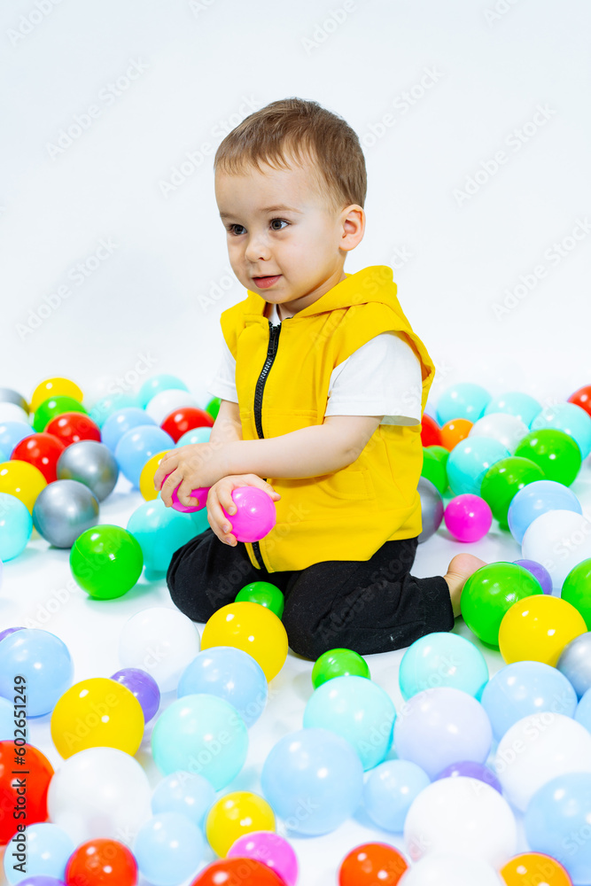 Obraz premium Playful boy having fun in playground. Little kid playing with colorful balls.