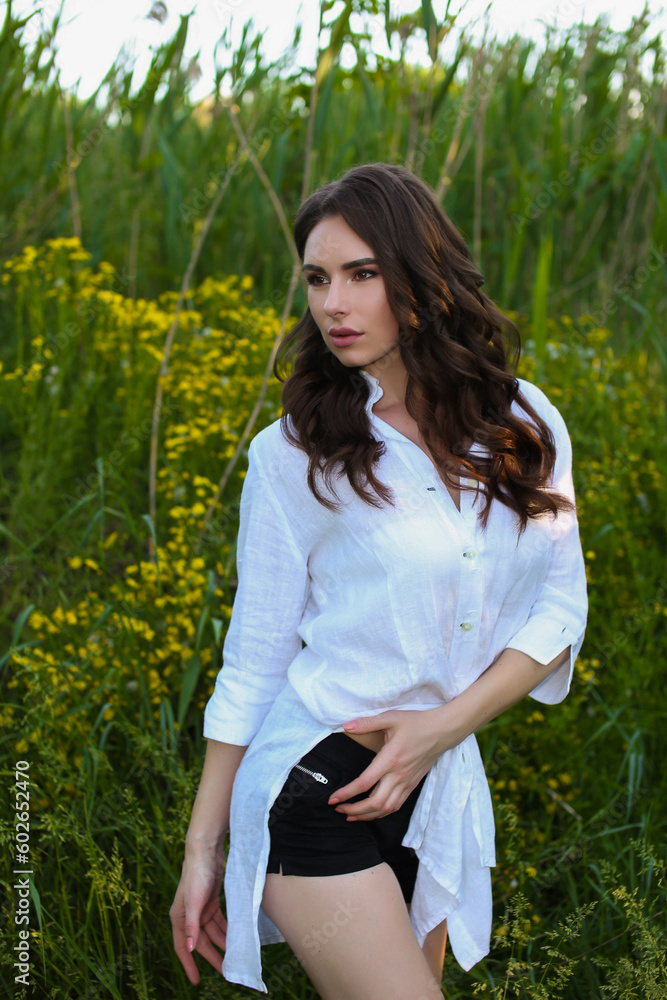 beautiful fashionable brunette woman adult posing in the park on the nature backgraund in white linen shirt beautiful fashionable brunette woman adult posing in the park on the nature backgraund in white linen shirt