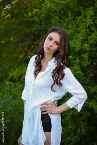 beautiful fashionable brunette woman adult posing in the park on the nature backgraund in white linen shirt