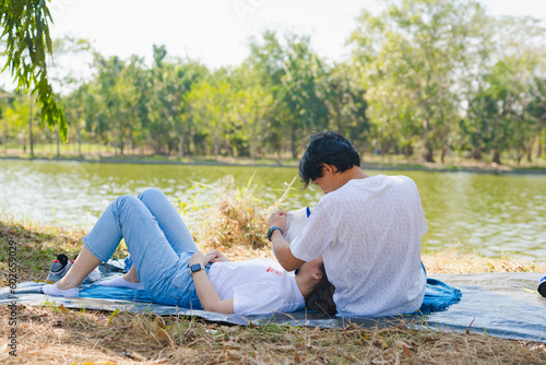asian couple picnic and relax with happiness feeling in park with lake in springtime