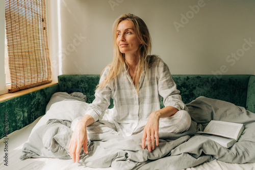 Beautiful woman in pajamas is sitting on the bed in the morning.