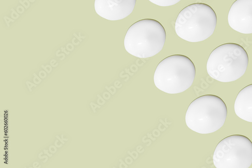 Lots of smears of cosmetic cream. Light  smooth surface.  In a row. At an angle. Top view. Texture of flowing cream. Liquid creamy strokes. On green background. Cosmetic background  banner.