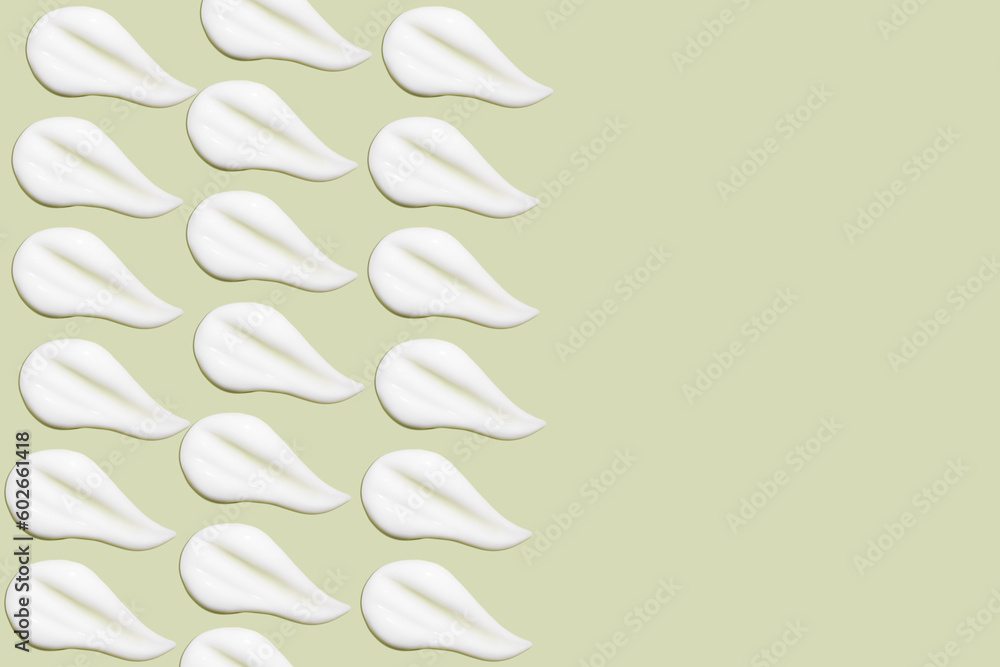 Lots of smears of cosmetic cream. Light, smooth surface. In a row. At an angle. Top view. Texture of flowing cream. Liquid creamy strokes. On green background. Cosmetic background, banner. Lots of smears of cosmetic cream. Light, smooth surface. In a row. At an angle. Top view. Texture of flowing cream. Liquid creamy strokes. On green background. Cosmetic background, banner.