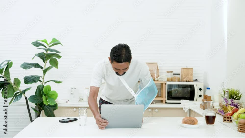man after an accident requiring arm braces helps arm recuperate better, talking on mobile phone in an unfamiliar manner, put phone on table bent down type on laptop computer one arm hit glass water. man after an accident requiring arm braces helps arm recuperate better, talking on mobile phone in an unfamiliar manner, put phone on table bent down type on laptop computer one arm hit glass water.