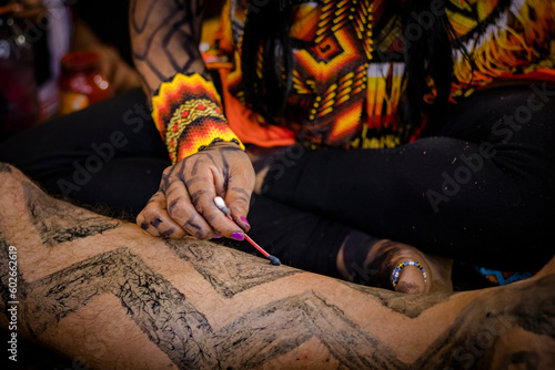 Sao Paulo, SP, Brazil - April 15 2023: Woman's hands with accessories and indigenous art doing traditional body painting of the culture with annatto and genipap details.