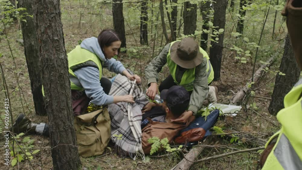 Tilt shot of Caucasian rescue team warming up and giving water to young male Biracial tourist lost in woods Tilt shot of Caucasian rescue team warming up and giving water to young male Biracial tourist lost in woods