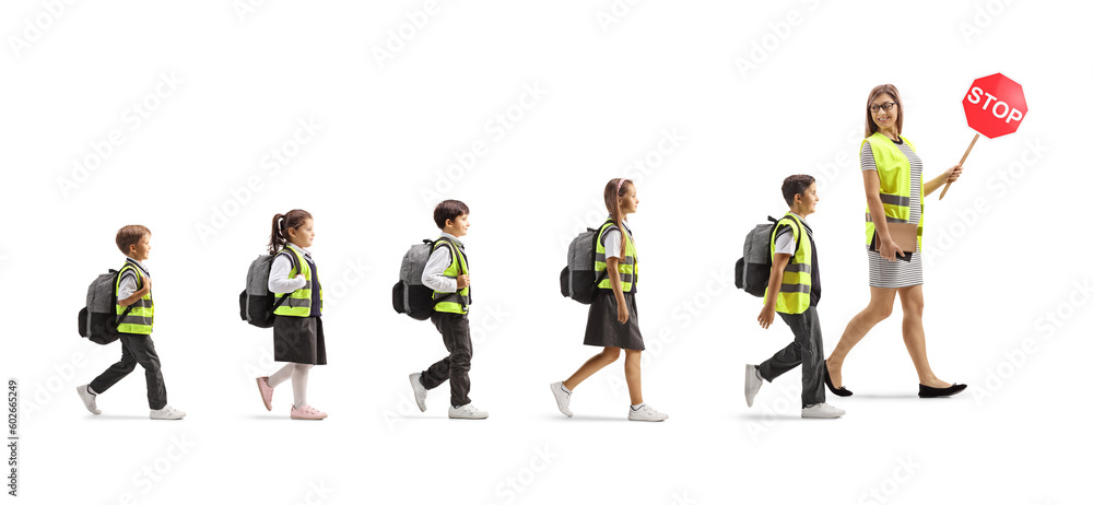Female teacher leading schoolchildren in safety vests, carrying a stop sign and walking