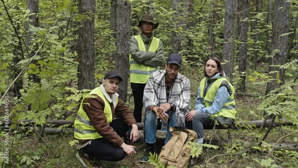 Portrait of young male Biracial tourist lost in forest and professional rescue team in acid green vests posing for camera in green woods Portrait of young male Biracial tourist lost in forest and professional rescue team in acid green vests posing for camera in green woods