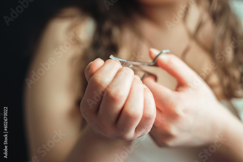 Young healthy woman at manicure cuts fingernail with nail metal scissors. Personal health care and beauty salon concept. Natural manicure with blurred background of the body.