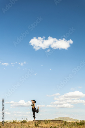 red-haired woman with outstretched arms in a meadow with white clouds and blue sky in the background © VICTOR