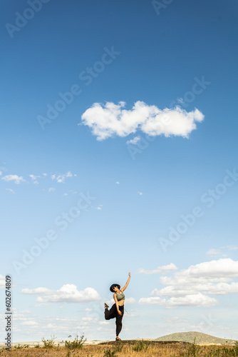 red-haired woman with outstretched arms in a meadow with white clouds and blue sky in the background