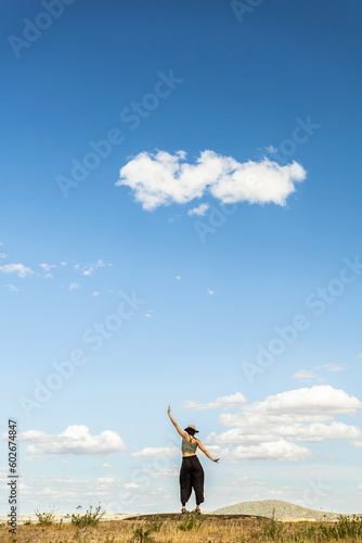 red-haired woman with outstretched arms in a meadow with white clouds and blue sky in the background