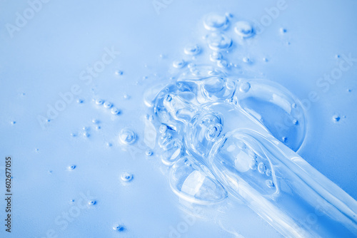Transparent cosmetic gel flows from an eyedropper directly onto the background in a large blob with bubbles. On a blue background. Hyaluronic acid  toner  toner  gel  cream. Cosmetics.