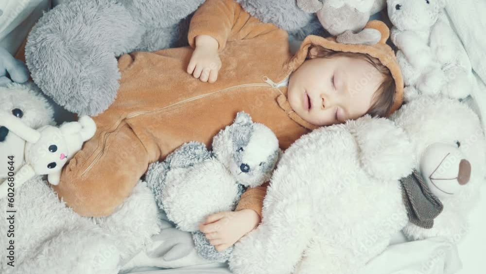 Little baby with outstretched hands lying in bed with fluffy stuffed toys of animals. Toddler sleeping with teddy bear in cozy room and enjoy healthy night sleep. Selective focus. Top view. Little baby with outstretched hands lying in bed with fluffy stuffed toys of animals. Toddler sleeping with teddy bear in cozy room and enjoy healthy night sleep. Selective focus. Top view.