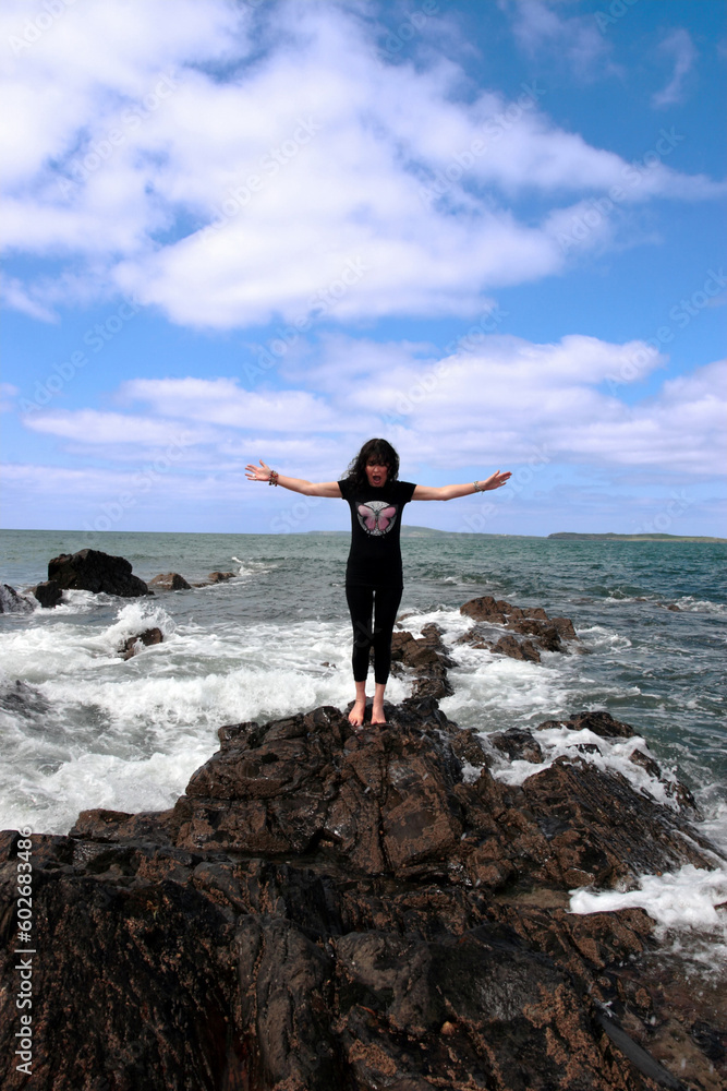 a beautiful woman doing yoga on the edge of the rocks with waves splashing to show a healthy way to live a happy and relaxed lifestyle in a world full of stress a beautiful woman doing yoga on the edge of the rocks with waves splashing to show a healthy way to live a happy and relaxed lifestyle in a world full of stress