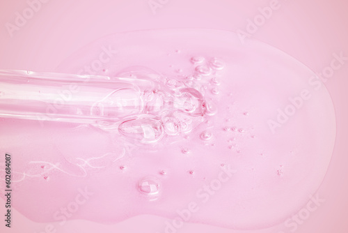 A flowing clear gel from a pipette. A lot of flowing gel in a big drop. With bubbles. On a pink background.