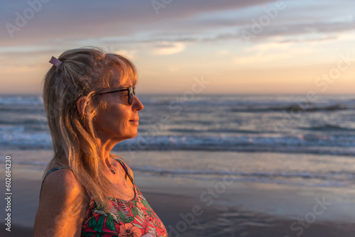 Relaxed mature woman with sunglasses enjoying the sunset on the beach.