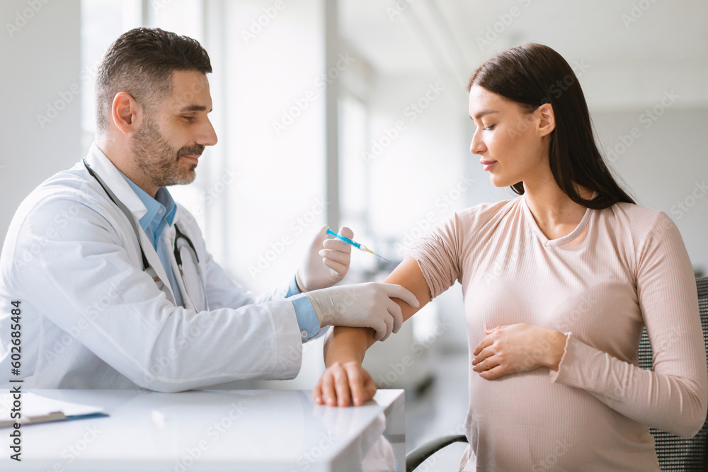 Injection against virus for risk groups. Male doctor making shot to young pregnant lady in clinic office Injection against virus for risk groups. Male doctor making shot to young pregnant lady in clinic office