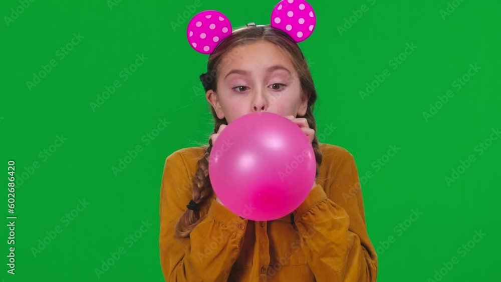 Closeup teen girl blowing pink balloon looking at camera at green screen. Cheerful Caucasian teenager celebrating birthday posing at chroma key background close-up