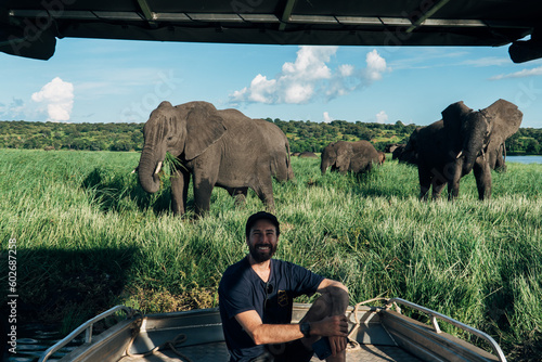 White, male, New Zealander on boat safari with elephants in the background in Chobe National Park in Botswana. 