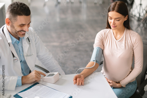 Therapist man checking hypertension of young expectant woman, measuring blood pressure for young pregnant patient © Prostock-studio