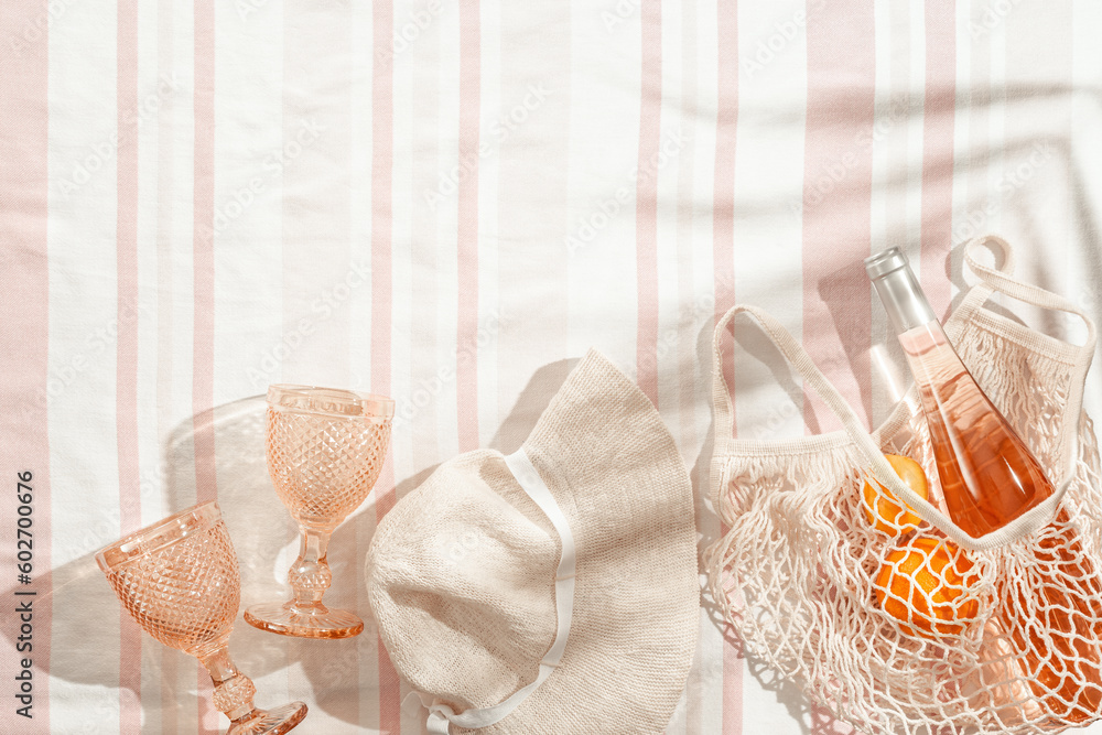 Φωτογραφία Summer pastel background with sun hat, wine glasses, bottle rose wine, orange fruits in mesh bag on stripes beach towel as background, shadows of palm leaves