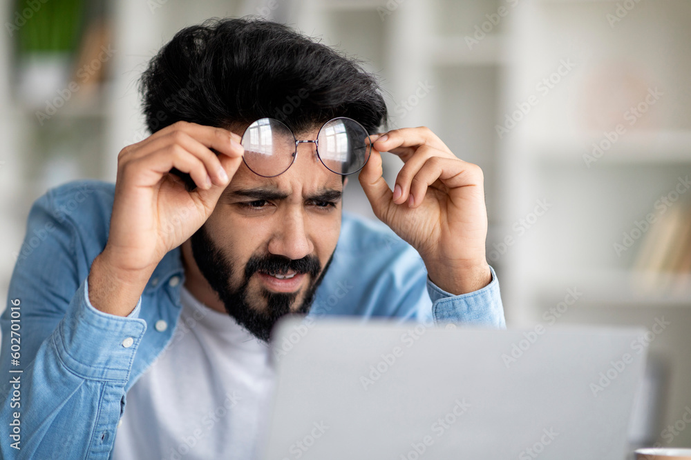 Error. Confused Indian Man Looking At Laptop Screen And Taking Off Eyeglasses Error. Confused Indian Man Looking At Laptop Screen And Taking Off Eyeglasses