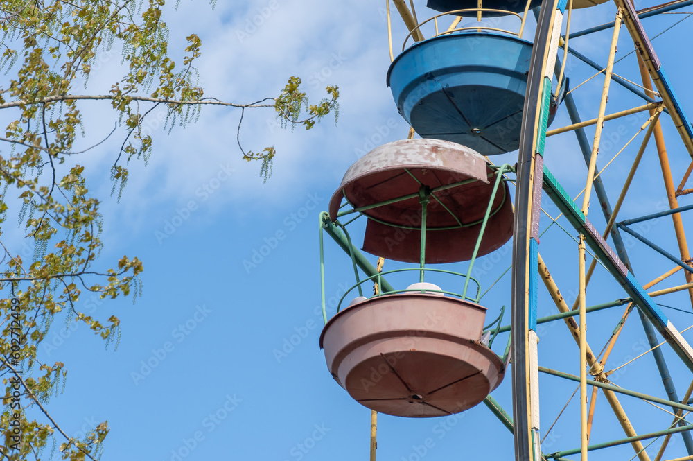 Old colorful ferris wheel in amusement park. Multicolour soviet carousel on blue sky background. Entertainment tall circle rotate in city. Round attractions of holiday for family. Traditional leisure. Old colorful ferris wheel in amusement park. Multicolour soviet carousel on blue sky background. Entertainment tall circle rotate in city. Round attractions of holiday for family. Traditional leisure.