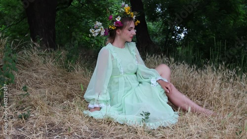 Fairytale character. Beautiful girl with wildflower crown and in green  dress sits in forest among trees. Paganism. Forest spirit, mavka, fairy. 4K Resolution
