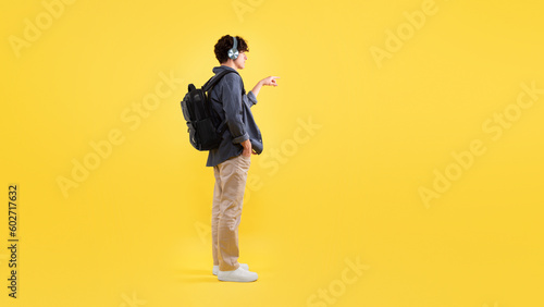 Man With Backpack Wearing Headphones Showing Free Space, Yellow Background © Prostock-studio