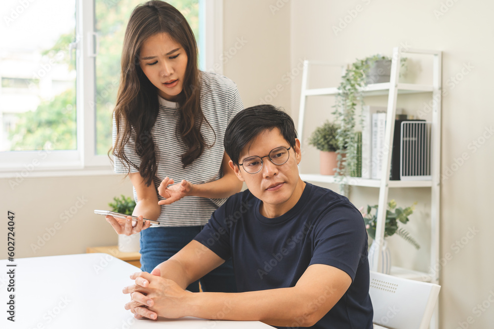 Infidelity, suspicion asian young couple love fight relationship, wife holding cellphone, smartphone cheating on phone, scolding husband about mistrust, distrust and jealousy when sitting at home. Infidelity, suspicion asian young couple love fight relationship, wife holding cellphone, smartphone cheating on phone, scolding husband about mistrust, distrust and jealousy when sitting at home.