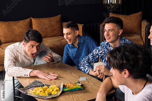 Five friends spending time together, having fun, playing table games and eating fast food and snacks. Small group of friend in a living room. man losing and raging at his friends.