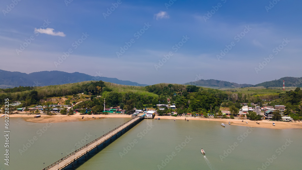 Long pier in the beautiful sea. Green water. Blue sky. Mountains in the distance. Tropical coast, colorful landscape.