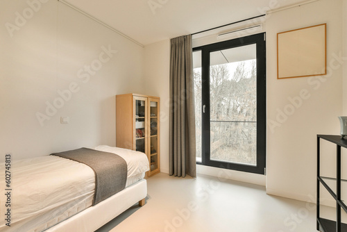 a bedroom with a bed, desk and large window looking out onto the trees in the photo is taken from inside