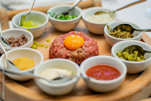 Fototapeta Naklejka Na Ścianę i Meble -  Restaurant waiter serving elaborate  - Beef tartare served on wooden board with various garnishes and egg yolk and person eats it