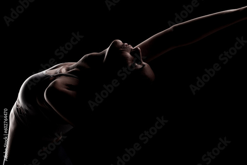 Beautiful caucasian girl posing yoga and stretching in shadow. side lit photo on black background.