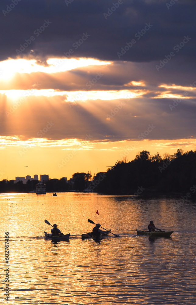 Group of people canoeing at sunset with sunrays shining through clouds Group of people canoeing at sunset with sunrays shining through clouds